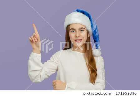 Smiling girl with blue Santa hat pointing up on white background. Smiling girl with blue Santa hat pointing up on white background. 131952386