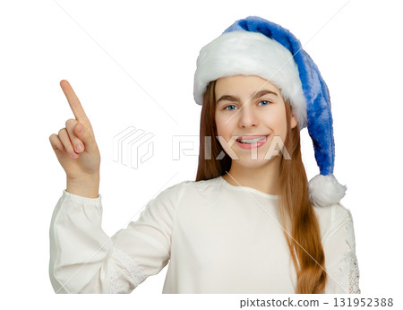 Smiling girl with blue Santa hat pointing up on white background. Smiling girl with blue Santa hat pointing up on white background. 131952388