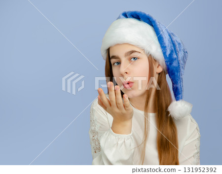 Smiling girl wearing blue and white Santa hat making heart shape with her hands,  131952392