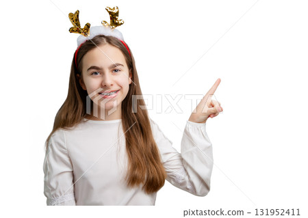 Smiling girl with sequin reindeer antlers pointing up on white background. Smiling girl with sequin reindeer antlers pointing up on white background. 131952411