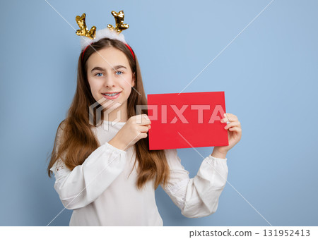 Teen girl with reindeer antler headband and long hair smiling while holding blank red card Teen girl with reindeer antler headband and long hair smiling while holding blank red card 131952413