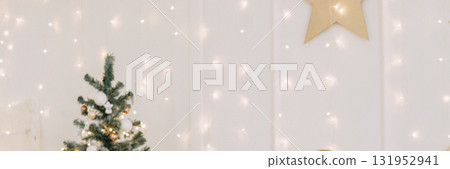 Decorated Christmas tree with shiny ornaments and fairy lights beside a wall with glowing bokeh. Festive holiday season interior design. Decorated Christmas tree with shiny ornaments and fairy lights beside a wall with glowing bokeh. Festive holiday season interior design. 131952941