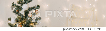 Decorated Christmas tree with shiny ornaments and fairy lights beside a wall with glowing bokeh. Festive holiday season interior design. Decorated Christmas tree with shiny ornaments and fairy lights beside a wall with glowing bokeh. Festive holiday season interior design. 131952943