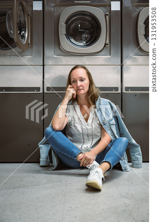 Woman sitting on floor in self service laundromat while waiting laundry 131953508