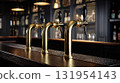 Three golden taps are aligned on a bar, backed by a blurred display of bottles, suggesting a pub or bar atmosphere. 131954143