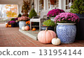 Fall porch decor featuring colorful mums and pumpkins. Cozy autumn scene. Potted flowers and gourds create a welcoming atmosphere. 131954144