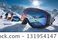 Ski goggles reflect a snowy mountain scene, with skiers in the background. The sun shines brightly above a crisp, clear, blue sky. 131954147