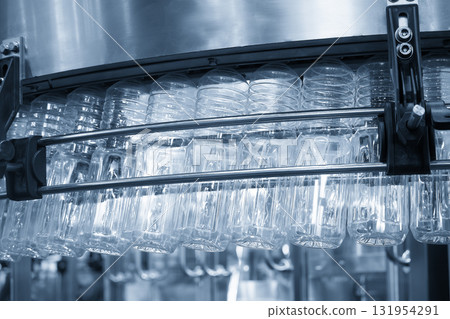 The empty drinking water bottles hanging on the overhead conveyor belt for filling process in the light blue scene. The empty drinking water bottles hanging on the overhead conveyor belt for filling process in the light blue scene. 131954291