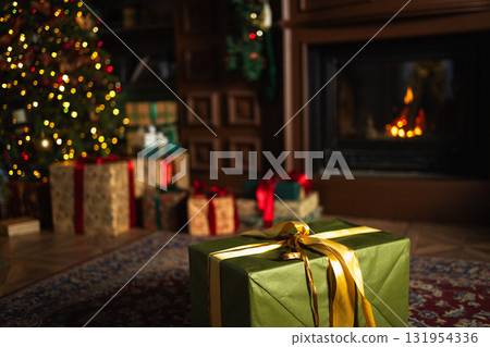 Green gift box in classical Christmas decorated interior living room library with fireplace. Christmas gift near fir tree on Christmas eve. Modern classic style interior design apartment. Christmas Green gift box in classical Christmas decorated interior living room library with fireplace. Christmas gift near fir tree on Christmas eve. Modern classic style interior design apartment. Christmas 131954336