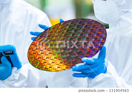 Male and female workers in protective clothing holding tablets and inspecting silicon wafers in a semiconductor factory Male and female workers in protective clothing holding tablets and inspecting silicon wafers in a semiconductor factory 131954563