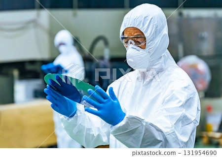 Male worker in protective clothing inspecting silicon wafers in a semiconductor factory Male worker in protective clothing inspecting silicon wafers in a semiconductor factory 131954690