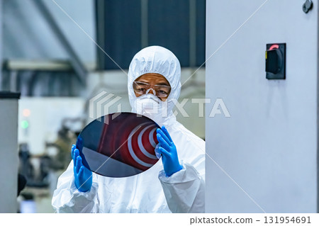 A female worker in protective clothing inspects silicon wafers in a semiconductor factory A female worker in protective clothing inspects silicon wafers in a semiconductor factory 131954691