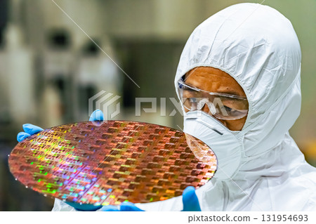 Male worker in protective clothing inspecting silicon wafers in a semiconductor factory Male worker in protective clothing inspecting silicon wafers in a semiconductor factory 131954693