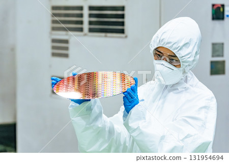 A female worker in protective clothing inspects silicon wafers in a semiconductor factory 131954694