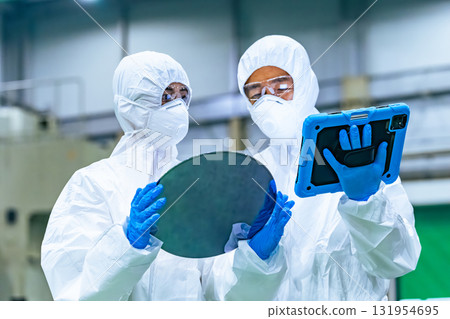Male worker in protective clothing inspecting silicon wafers in a semiconductor factory Male worker in protective clothing inspecting silicon wafers in a semiconductor factory 131954695