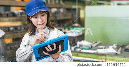 A female worker inspecting factory machinery with a tablet 131954731