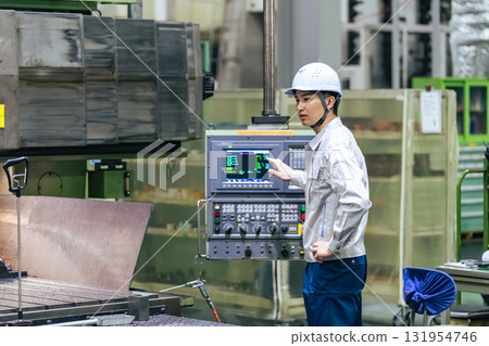A male worker operates a machine on a control panel in a factory A male worker operates a machine on a control panel in a factory 131954746