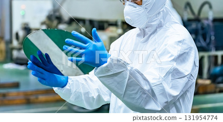 Male worker in protective clothing inspecting silicon wafers in a semiconductor factory Male worker in protective clothing inspecting silicon wafers in a semiconductor factory 131954774