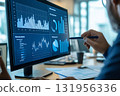 Business analyst is pointing at a graph on a computer screen with a pen, analyzing financial data 131956336