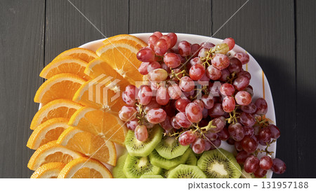 A plate of fruit with oranges, kiwis, and grapes 131957188