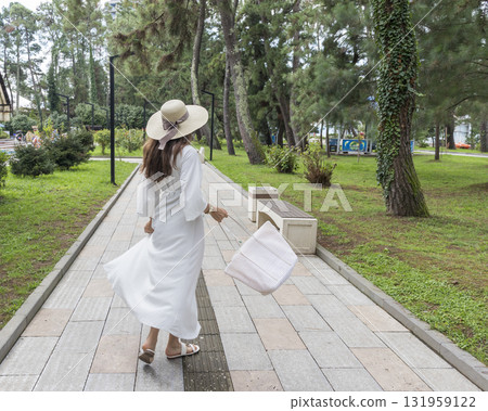 Woman with long brown hair, in white outfit walks her dog in the park Woman with long brown hair, in white outfit walks her dog in the park 131959122