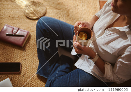 Cozy Home Tea Moment: Woman Sitting On Rug, Jeans, White Shirt, Enjoying Hot Lemon Tea 131960003