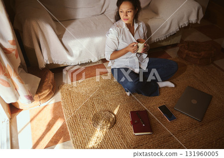Cozy Morning At Home: Woman Sits On Rug With Coffee, Laptop, And Phone 131960005