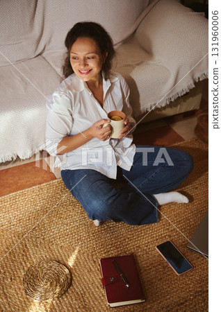 Cozy Home Morning: Woman Sits On Rug With Coffee Mug, Laptop Nearby, Smiling And Relaxed Cozy Home Morning: Woman Sits On Rug With Coffee Mug, Laptop Nearby, Smiling And Relaxed 131960006