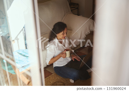 Woman Working From Home With Laptop And Coffee Mug In Cozy Living Space Woman Working From Home With Laptop And Coffee Mug In Cozy Living Space 131960024
