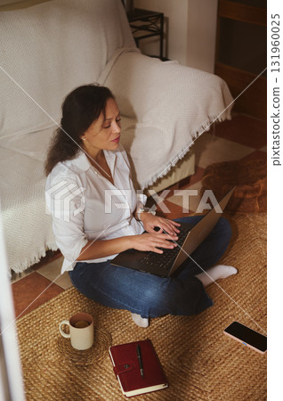 Focused Woman Working From Home With Laptop, Notebook, And Coffee In Cozy Living Room Focused Woman Working From Home With Laptop, Notebook, And Coffee In Cozy Living Room 131960025
