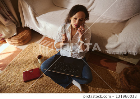 Woman Working From Home On Laptop While Talking On Phone In Cozy Living Room 131960038