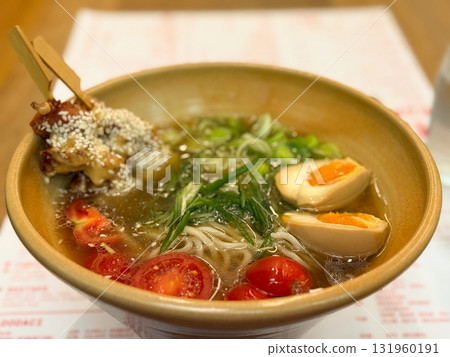 A bowl of ramen with egg, cherry tomatoes and sesame chicken. Asian cuisine, comfort food and dining experience representing balance, flavor and culinary aesthetics. A bowl of ramen with egg, cherry tomatoes and sesame chicken. Asian cuisine, comfort food and dining experience representing balance, flavor and culinary aesthetics. 131960191