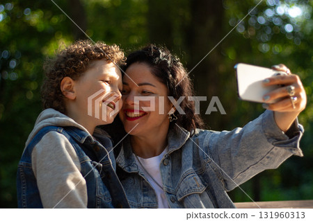 Mother making selfie together with her son. Taking selfie on smartphone. Smiling happy young family make photos outside in park to memorize moment. 131960313
