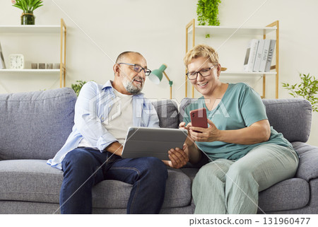 Senior couple using tablet and smartphone on sofa, learning digital skills Senior couple using tablet and smartphone on sofa, learning digital skills 131960477