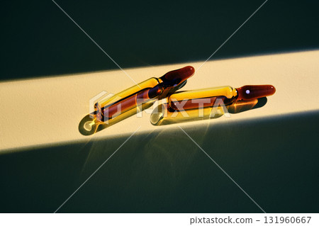 Two ampoules of hair serum in a beam of light on a beige background. Two ampoules of hair serum in a beam of light on a beige background. 131960667