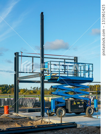 Blue scissor lift at construction site with steel frame structure under clear blue sky Blue scissor lift at construction site with steel frame structure under clear blue sky 131961425