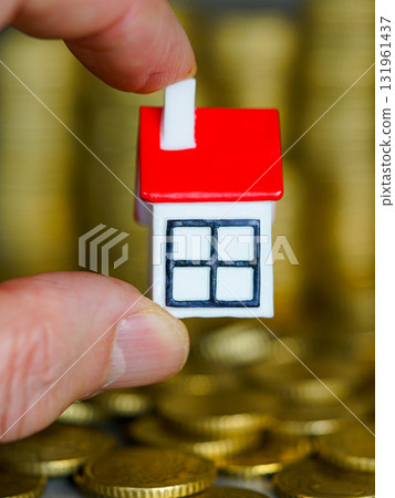 Hand holding small house model above gold coins symbolizing real estate, mortgage, and investment Hand holding small house model above gold coins symbolizing real estate, mortgage, and investment 131961437