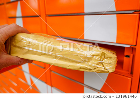 Hand placing a parcel into an orange parcel locker, symbolizing modern delivery and e-commerce 131961440