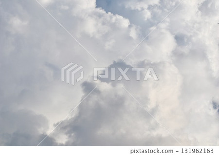 A detailed, closeup view of dense, towering cumulonimbus clouds, showing various shades of white and grey, suggesting heavy weather and dramatic atmospheric depth. 131962163