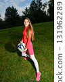 Young Woman in Sporty Outfit Holding Soccer Ball on a Grassy Field 131962289