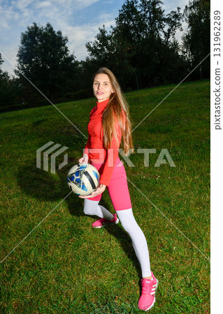 Young Woman in Sporty Outfit Holding Soccer Ball on a Grassy Field 131962289
