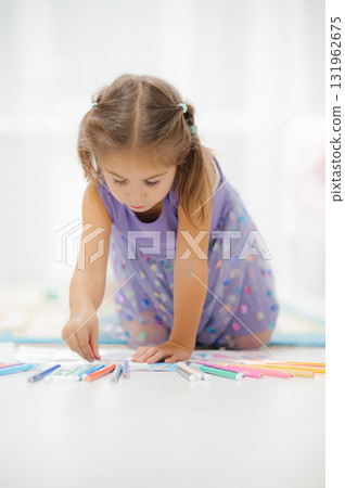 A Little Girl Enjoys Coloring with Bright Markers While Sitting on the Floor Nearby A Little Girl Enjoys Coloring with Bright Markers While Sitting on the Floor Nearby 131962675