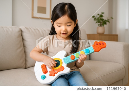 Child Plays With Colorful Toy Guitar in a Cozy Living Room During Daylight Hours 131963040