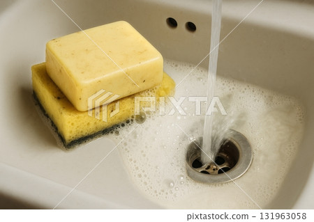 Soapy Sponge and Bar of Soap in Kitchen Sink With Running Water Creating Bubbles 131963058