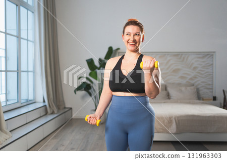 Fitness workout training. Woman picking up dumbbells. Plus size female doing sports exercise at home indoor. Girl in sportswear have workout weight training for weight loss. Sport and fitness 131963303