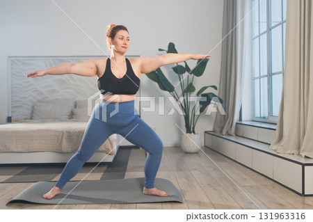 Yoga fitness workout training. Woman practicing yoga at home. Plus size female doing sports exercise on yoga mat indoor. Girl in sportswear have training workout for weight loss. Sport and fitness 131963316
