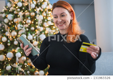Christmas shopping. Woman shopping online holding smartphone paying with gold credit card for Christmas presents gifts. Girl buying on Internet enter credit card details. Christmas winter holidays Christmas shopping. Woman shopping online holding smartphone paying with gold credit card for Christmas presents gifts. Girl buying on Internet enter credit card details. Christmas winter holidays 131963326