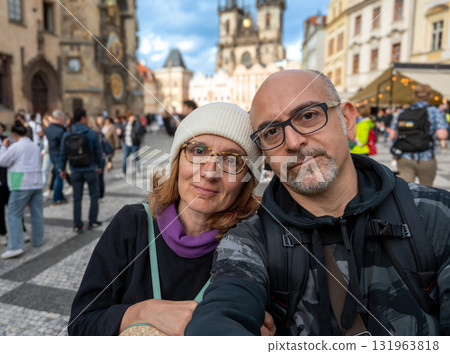 Prague, Czech Republic, August 7, 2023. A middle-aged couple takes a selfie in the iconic, crowded Old Town Square. Blurred background, travel destinations. 131963818