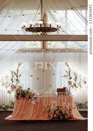 Elegant wedding sweetheart table with peach drapery and floral decorations in bright hall 131963941