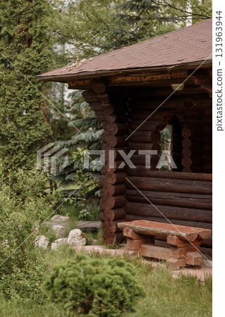 Wooden log gazebo with bench surrounded by green trees and grass in summer garden 131963944